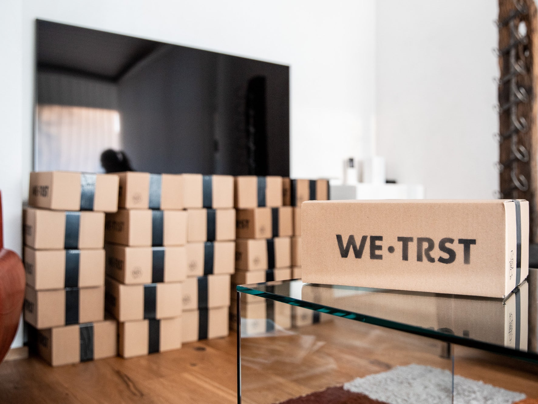 Das Bild zeigt viele versandbereite Pakete von WE•TRST. Die Pakete sind in einem Raum aufeinander gestapelt. Jedes Paket ist mit dem Logo von WE•TRST versehen und ist bereit für den Versand an Kunden auf der ganzen Welt.