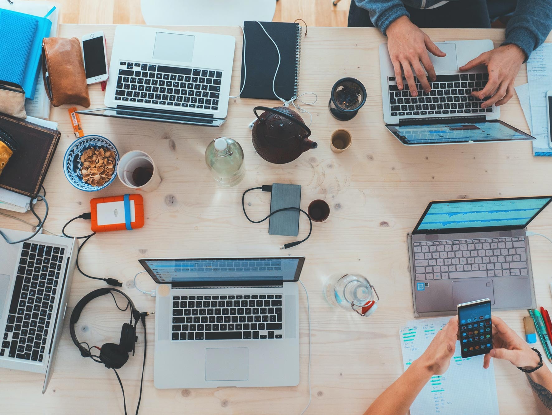 Das Bild zeigt einen Tisch mit verschiedenen Laptops und elektronischen Geräten. Es gibt mehrere Laptops mit verschiedenen Marken und Farben sowie weitere Geräte wie Tablets, Smartphones und Kopfhörer, die auf dem Tisch verteilt sind.