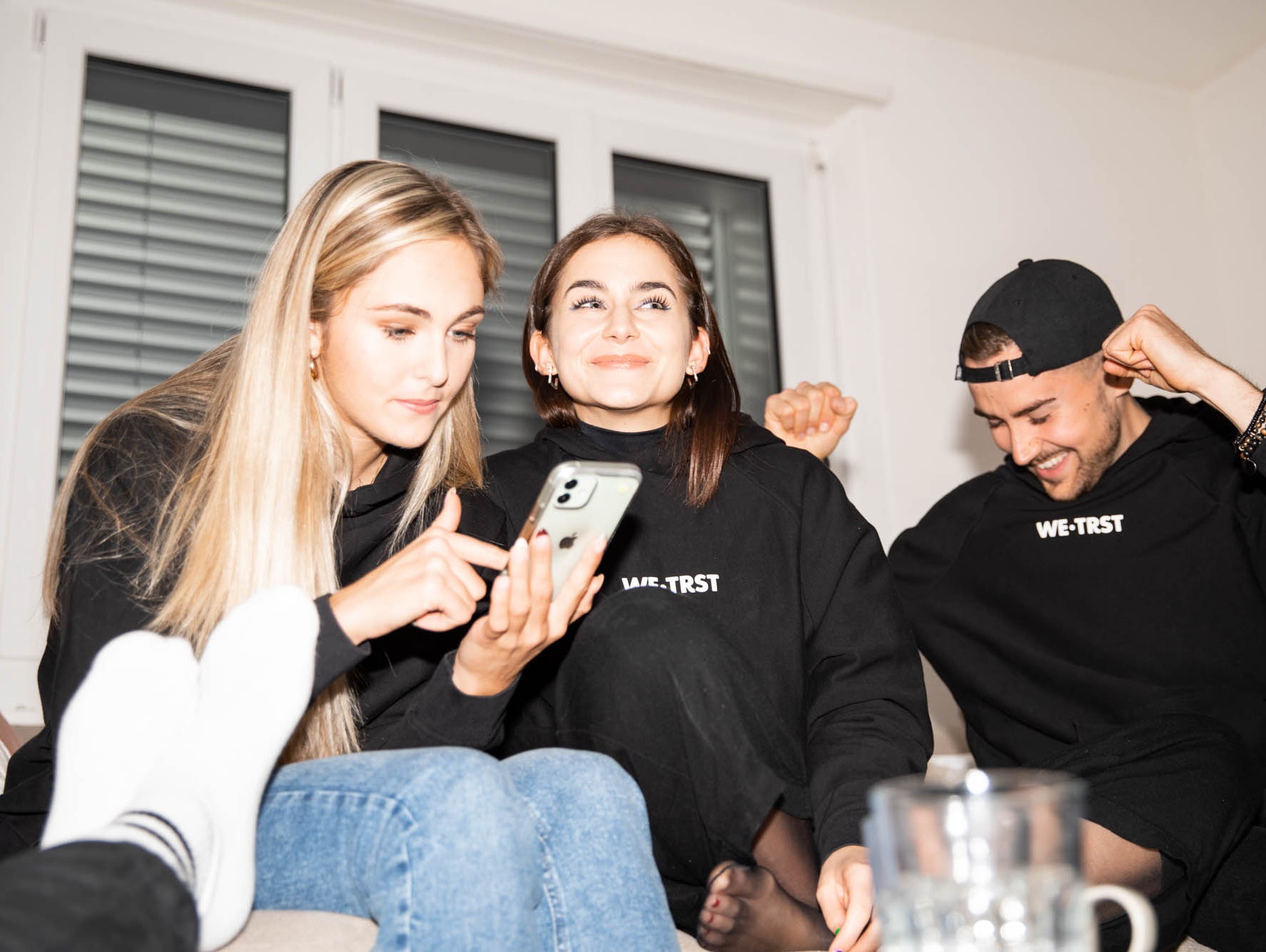Das Bild zeigt drei Teammitglieder von WE•TRST, die zusammenarbeiten und Spass haben. Sie sitzen auf einem Sofa und arbeiten an einem Projekt, wobei sie verschiedene Dokumente und Technologiegeräte verwenden.