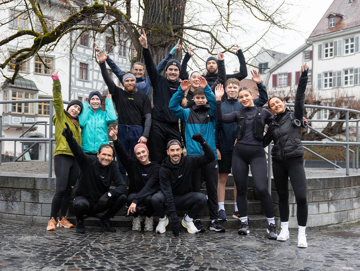 Group of enthusiastic runners from the WETRST Run Club posing together in a European city square after a community workout session.