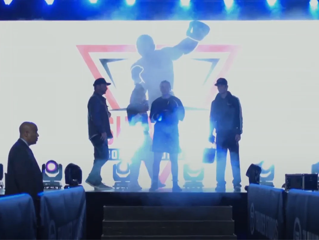 Julia Igel and team entering the arena with dramatic backlighting and fog, in front of a large boxing-themed LED screen during a professional event