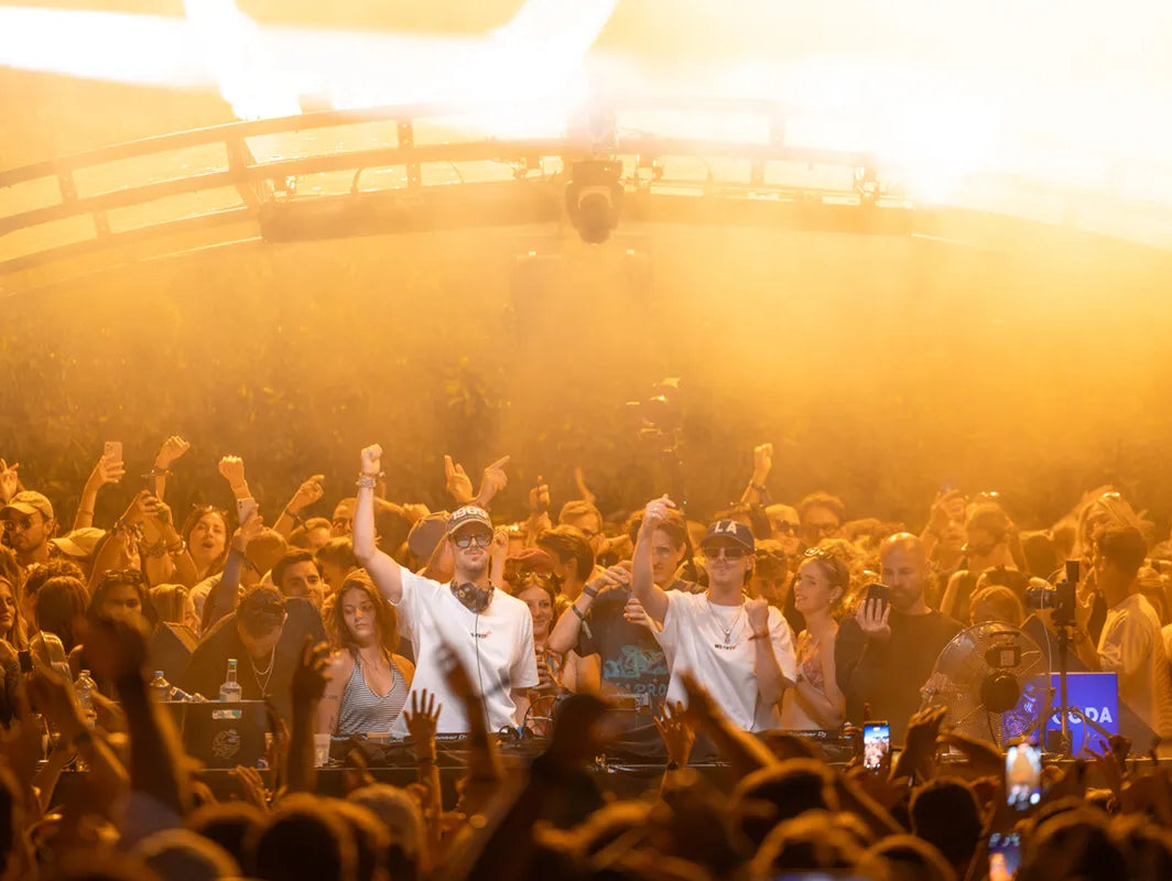Die Dangel Twins während ihres DJ-Sets am CODA Openair 2025, umgeben von tanzenden Menschen in WE•TRST Shirts, unter goldener Festivalbeleuchtung.