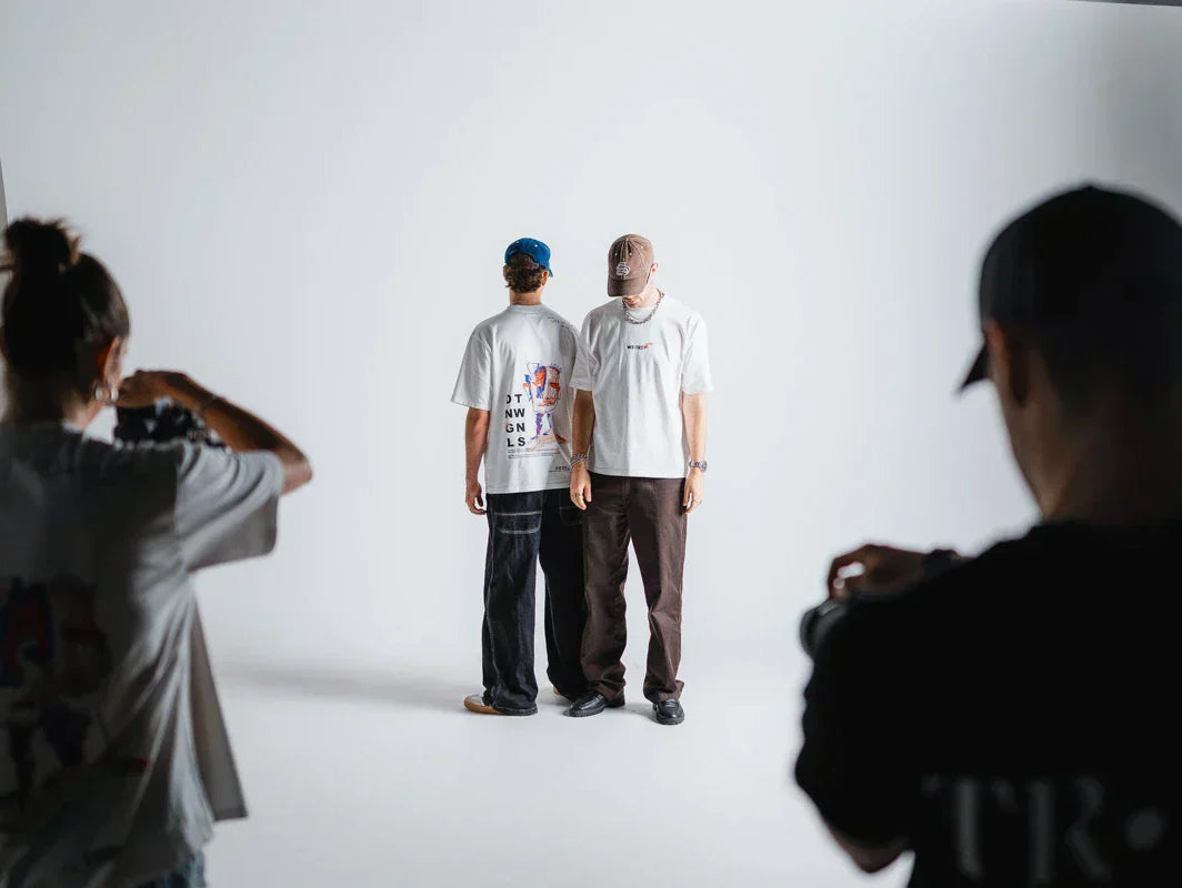 Fotoshooting der WE•TRST x Dangel Twins Kollektion im Studio – die Dangel Twins im Fokus, Fotograf:innen links und rechts, cleanes weisses Set mit Softbox.
