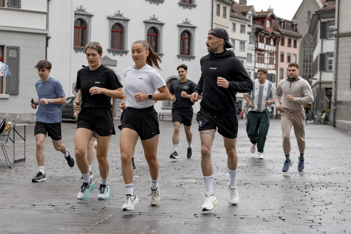 Läufer:innen des WE•TRST Run Clubs joggen durch die historische Altstadt von St. Gallen – Community Run bei bewölktem Wetter.