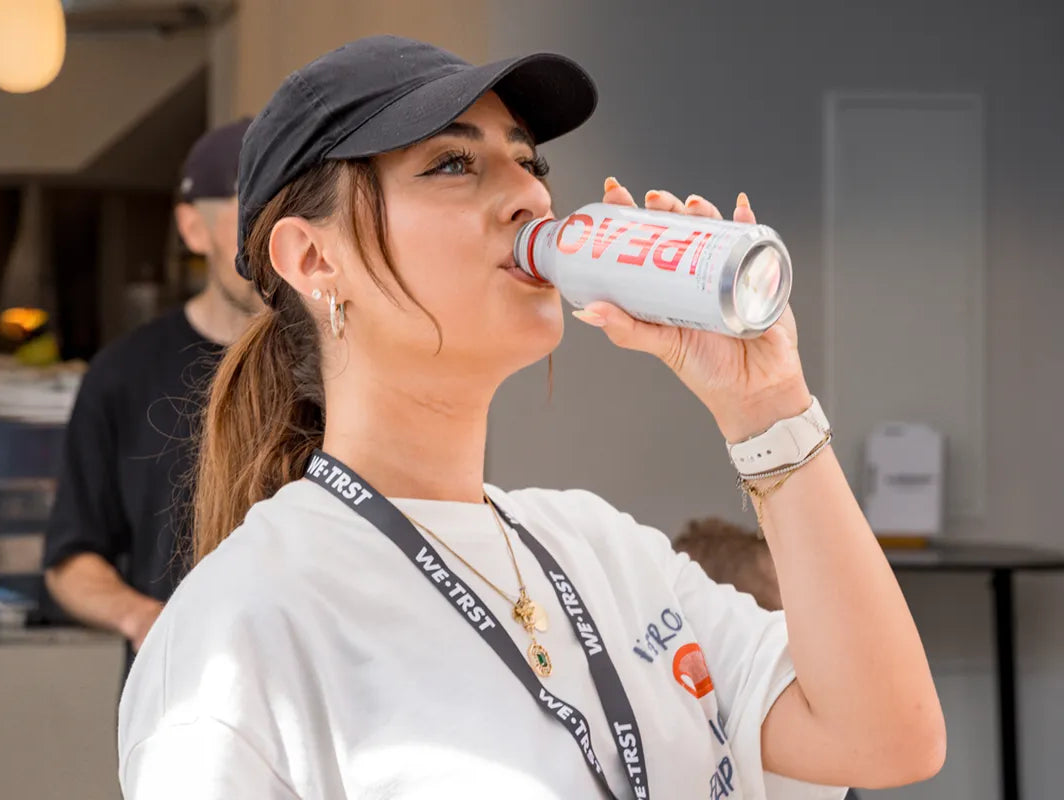 Frau mit WE•TRST-Shirt und Lanyard trinkt eine PEAQ Hydration Dose beim WE•TRST Run Club – Fokus auf Community, Sport und Schweizer Performance Water.