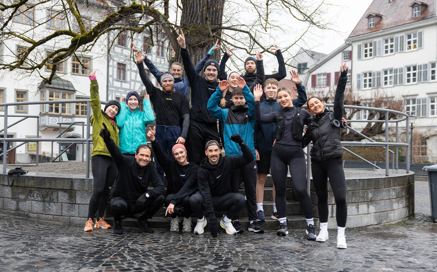 Eine Gruppe begeisterter Läufer des WE•TRST Run Club posiert nach einem gemeinsamen Training auf einem europäischen Stadtplatz.