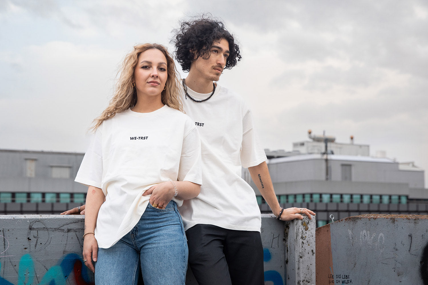 Zwei Models von WE•TRST stehen vor einem Urbanen Hintergrund mit dem neuen «Cloud Walker» T-Shirt modell.