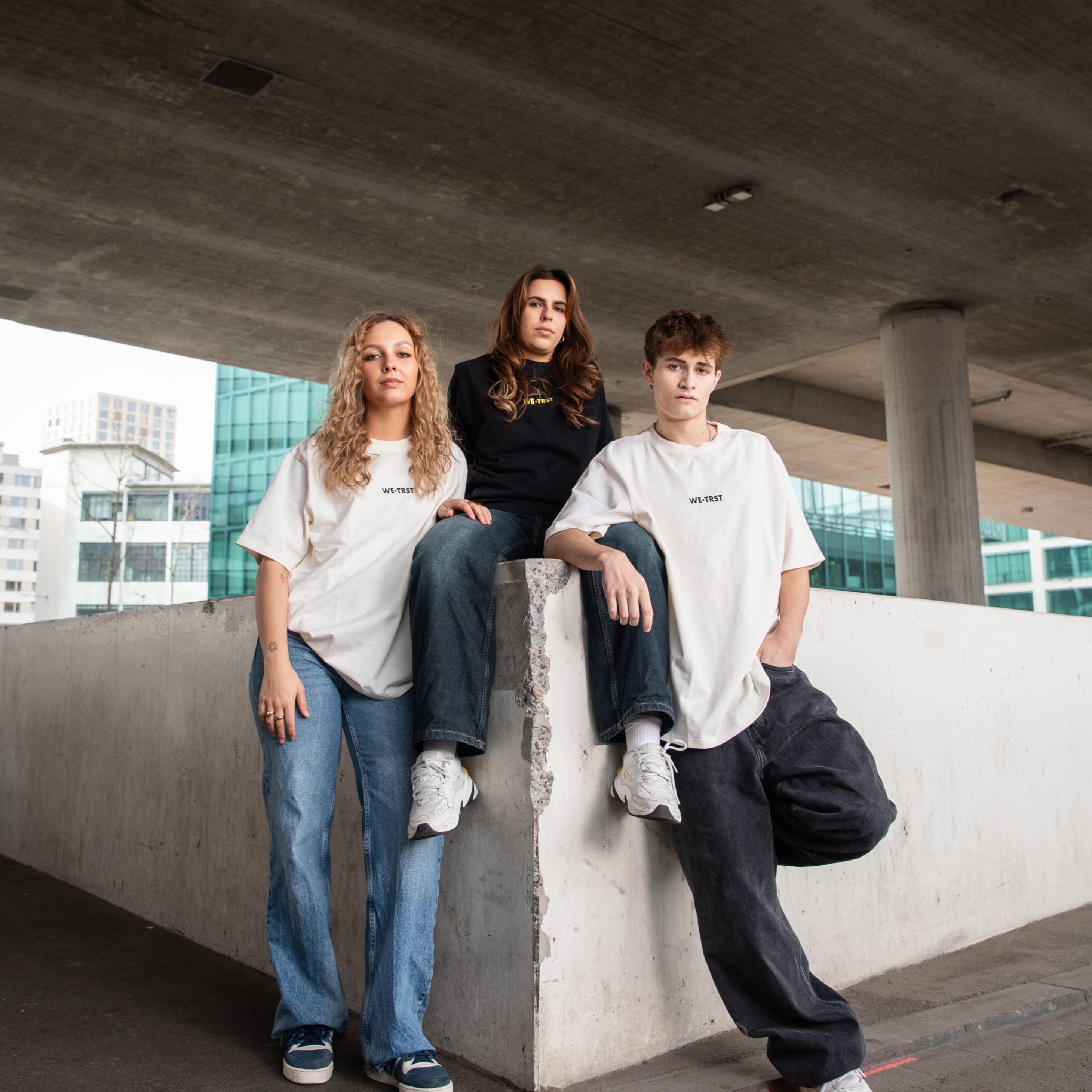 Drei Models in WE•TRST Streetwear unter einer Betonbrücke - Urban Fashion Editorial mit minimalistischer Ästhetik.