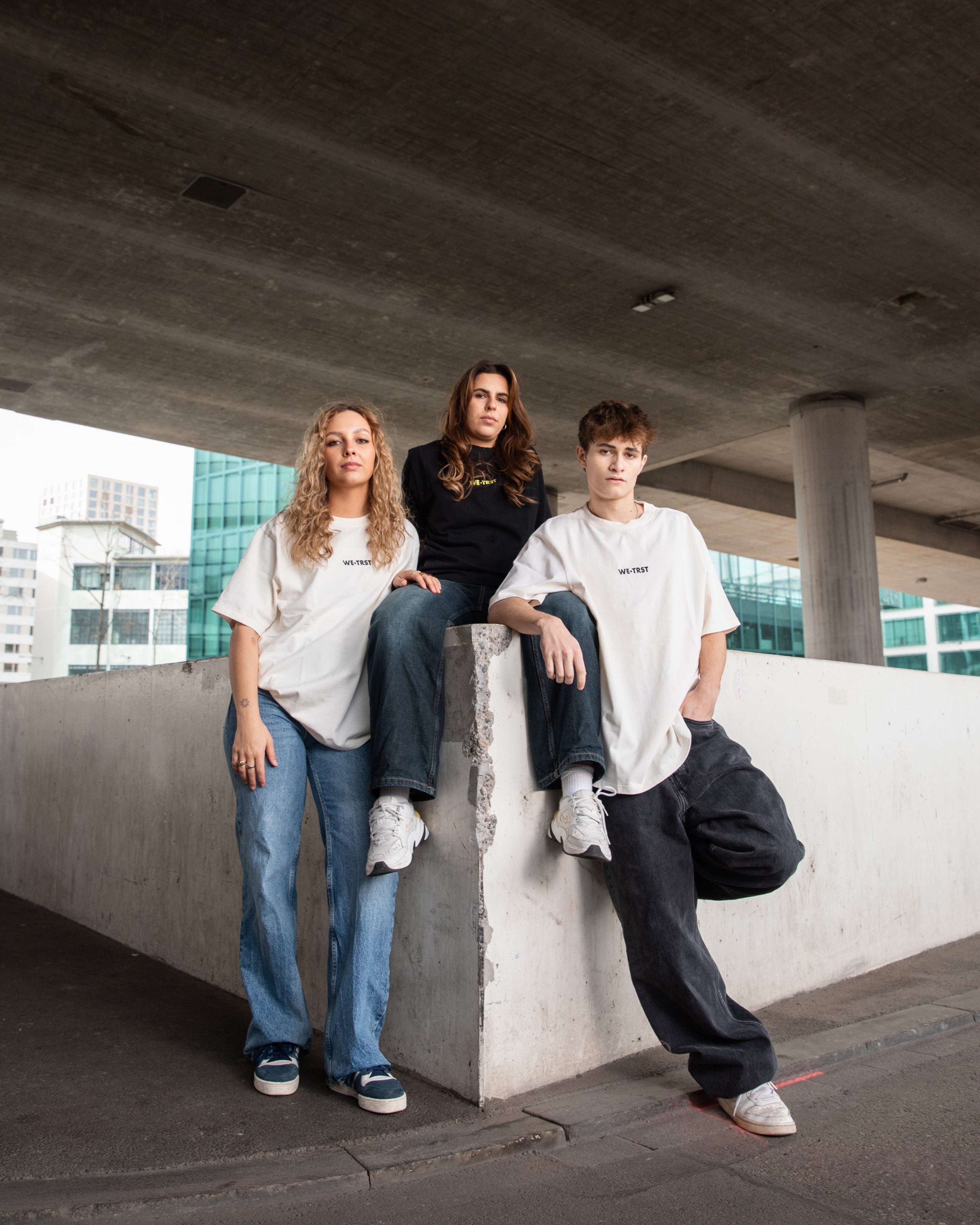 Drei Models in WE•TRST Streetwear unter einer Betonbrücke - Urban Fashion Editorial mit minimalistischer Ästhetik.