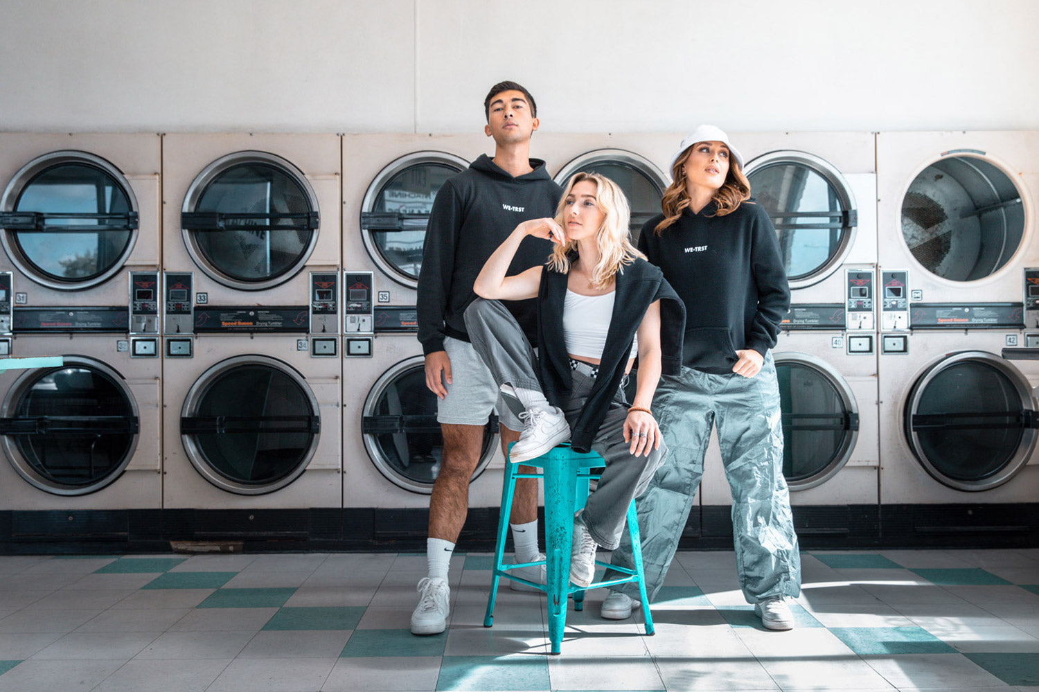 Die Models stehen stolz und motiviert im Waschraum und präsentieren ihre schwarzen Hoodies von WE•TRST.