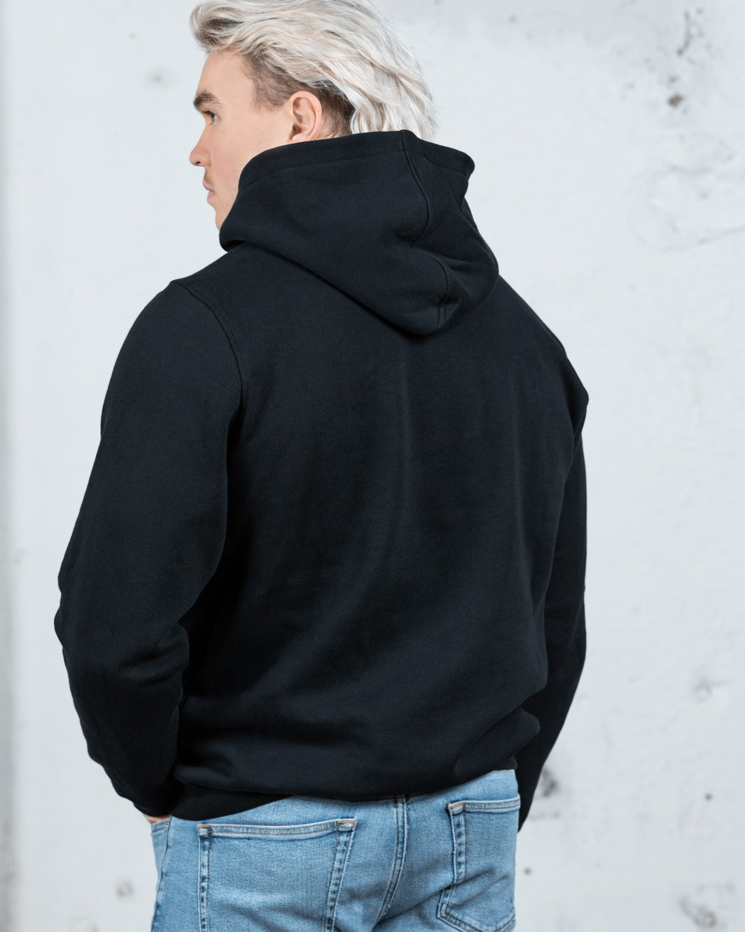 Rückenansicht eines männlichen Modells in einem schwarzen WE•TRST-Kapuzenpullover, wobei die übergroße Passform und das strukturierte Kapuzendesign hervorgehoben werden.