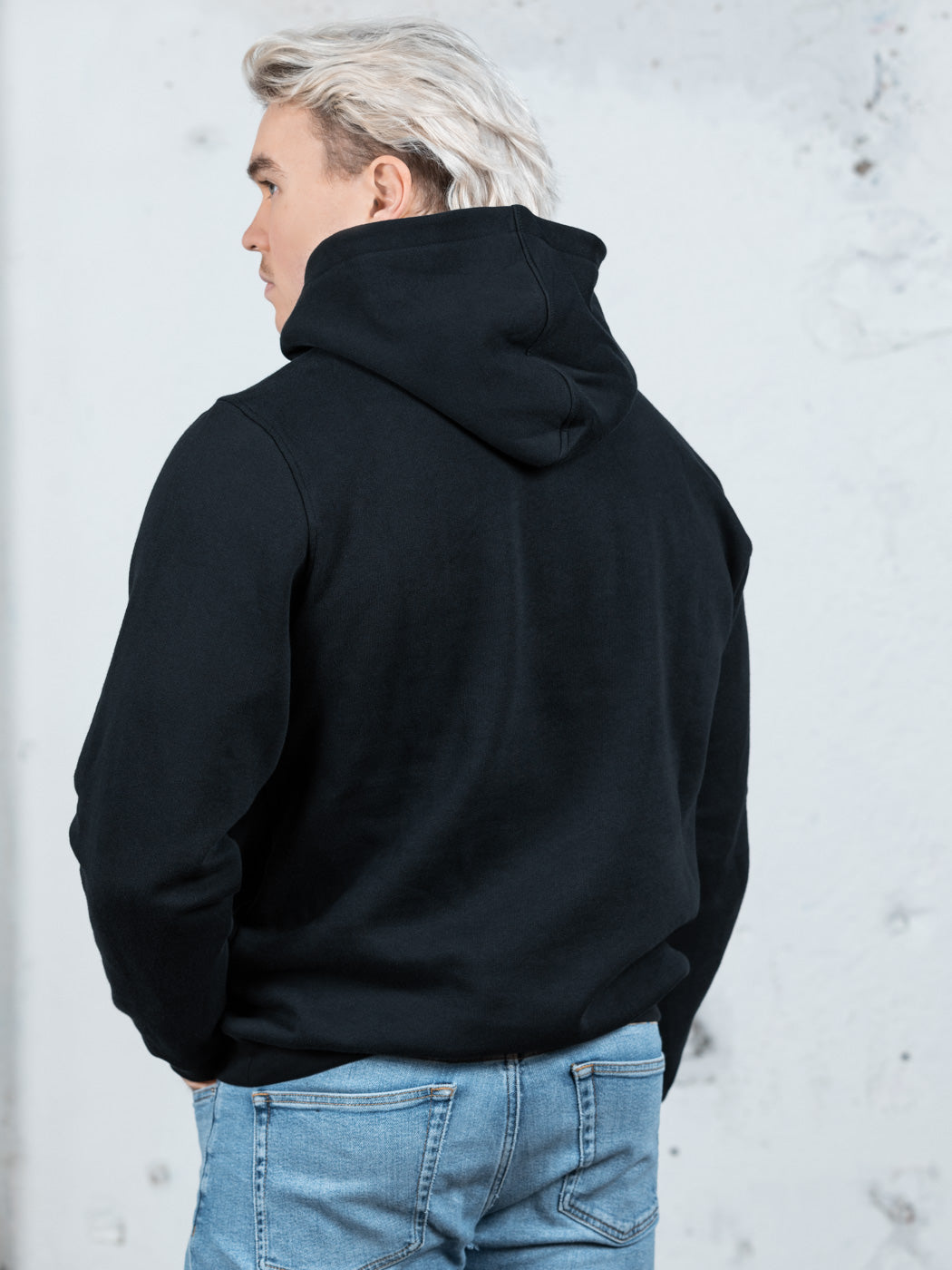 Rückenansicht eines männlichen Modells in einem schwarzen WE•TRST-Kapuzenpullover, wobei die übergroße Passform und das strukturierte Kapuzendesign hervorgehoben werden.