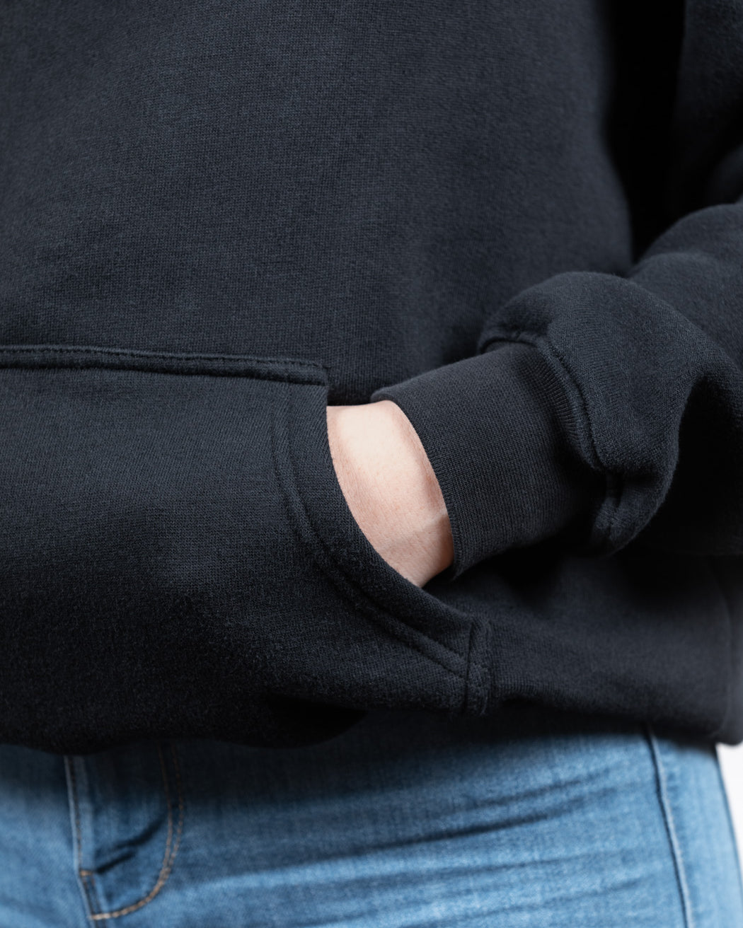 Nahaufnahme der Hand eines Models in der Tasche eines schwarzen WE•TRST-Kapuzenpullis, wobei der dicke Stoff und die hochwertigen Nähte besonders gut zur Geltung kommen.