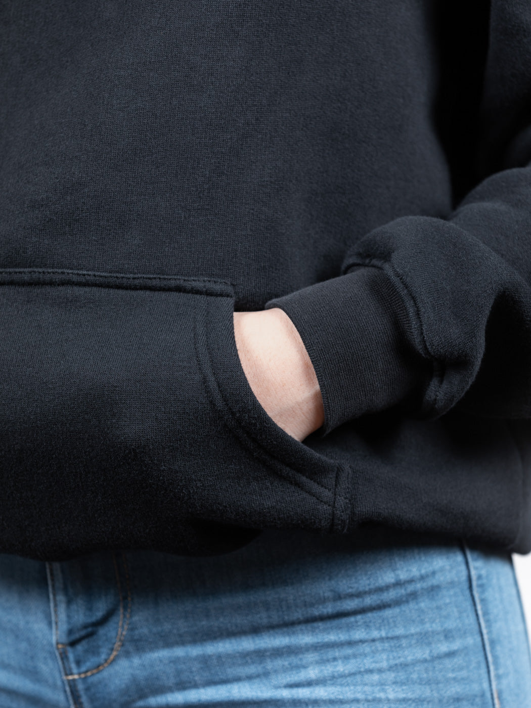 Nahaufnahme der Hand eines Models in der Tasche eines schwarzen WE•TRST-Kapuzenpullis, wobei der dicke Stoff und die hochwertigen Nähte besonders gut zur Geltung kommen.