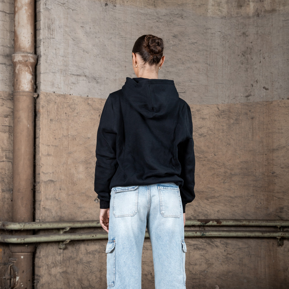 Rückenansicht eines weiblichen Models in einem schwarzen WE•TRST-Kapuzenpullover, der ein minimalistisches Design mit Kapuze und ohne zusätzliche Aufdrucke zeigt.