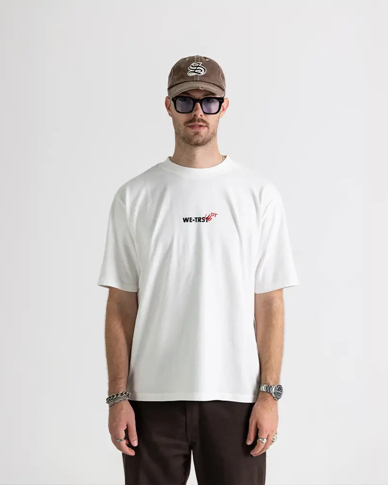 Chris Dangel von den Dangel Twins mit brauner Cap und Sonnenbrille trägt das weisse WE•TRST Dangel Twins-Shirt in Studio-Setting – Frontansicht.