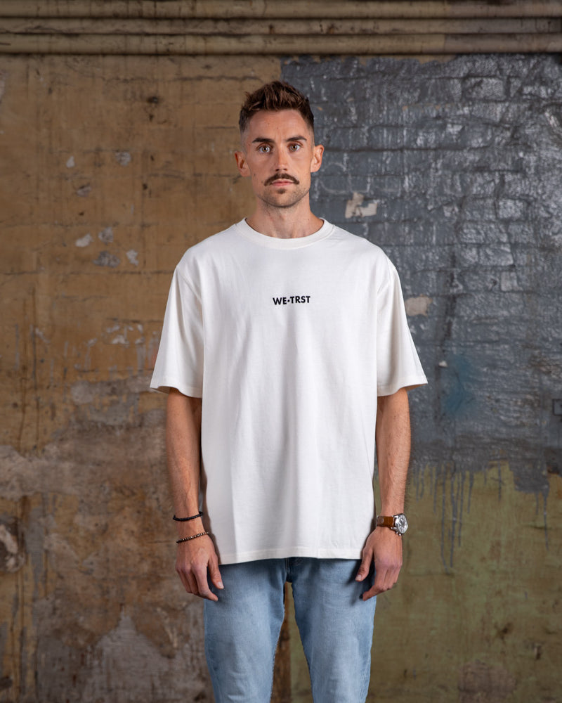 Vorderansicht des WE•TRST „Driven by Trust“ Oversized-T-Shirts in Off-White mit minimalistischem Branding und entspannter Passform.