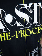 Detaillierte Nahaufnahme des gestickten „WE•TRST“-Logos in Gelb auf schwarzem Stoff, wobei die Textur und die Qualität der Nähte hervorgehoben werden.