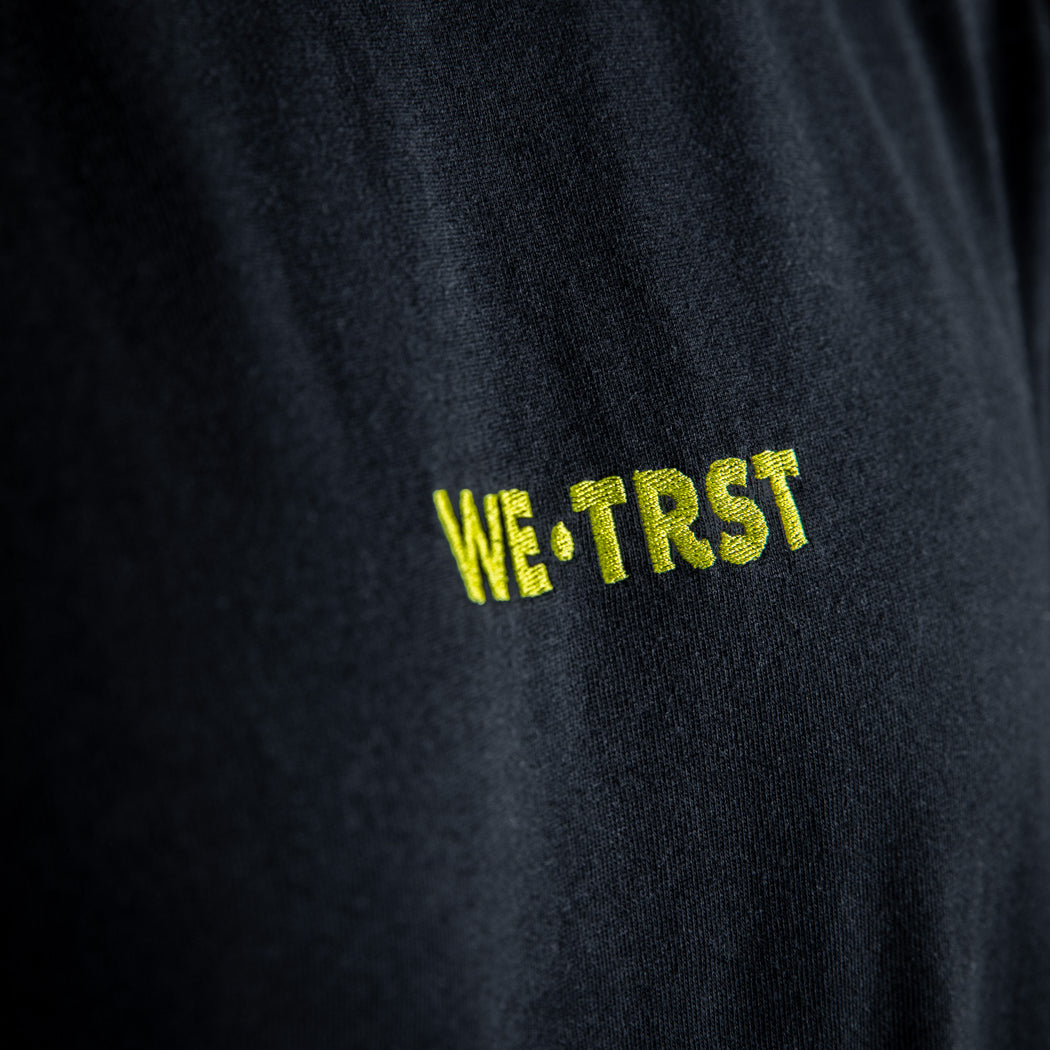 Nahaufnahme eines schwarzen WE•TRST T-Shirts mit Schwerpunkt auf dem weichen Stoff, der lockeren Passform und den kurzen Ärmeln.