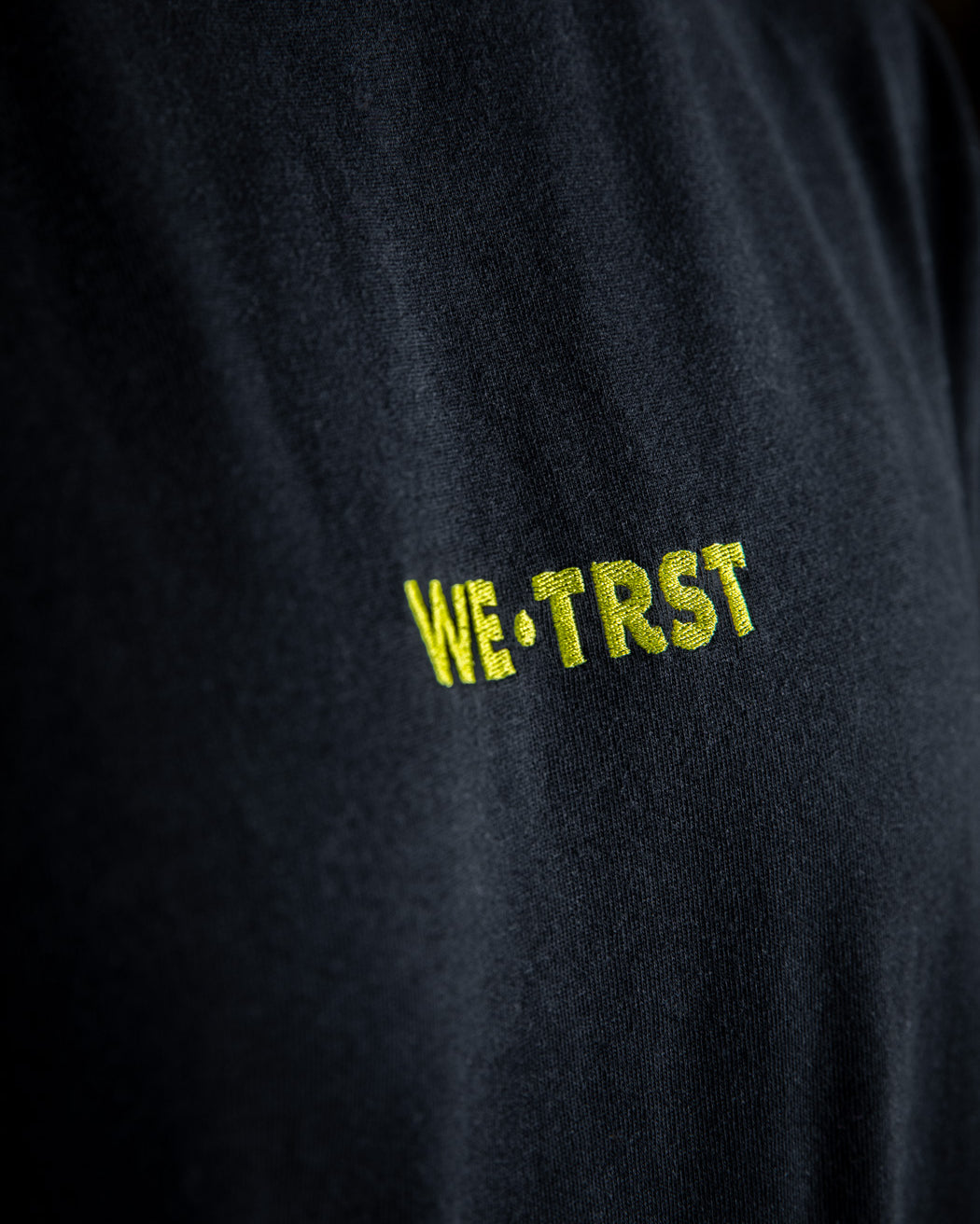 Nahaufnahme eines schwarzen WE•TRST T-Shirts mit Schwerpunkt auf dem weichen Stoff, der lockeren Passform und den kurzen Ärmeln.