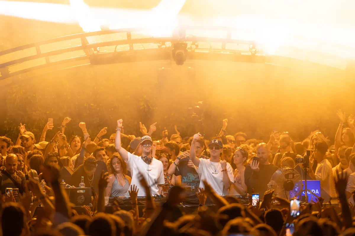 Die Dangel Twins während ihres DJ-Sets am CODA Openair 2025, umgeben von tanzenden Menschen in WE•TRST Shirts, unter goldener Festivalbeleuchtung.