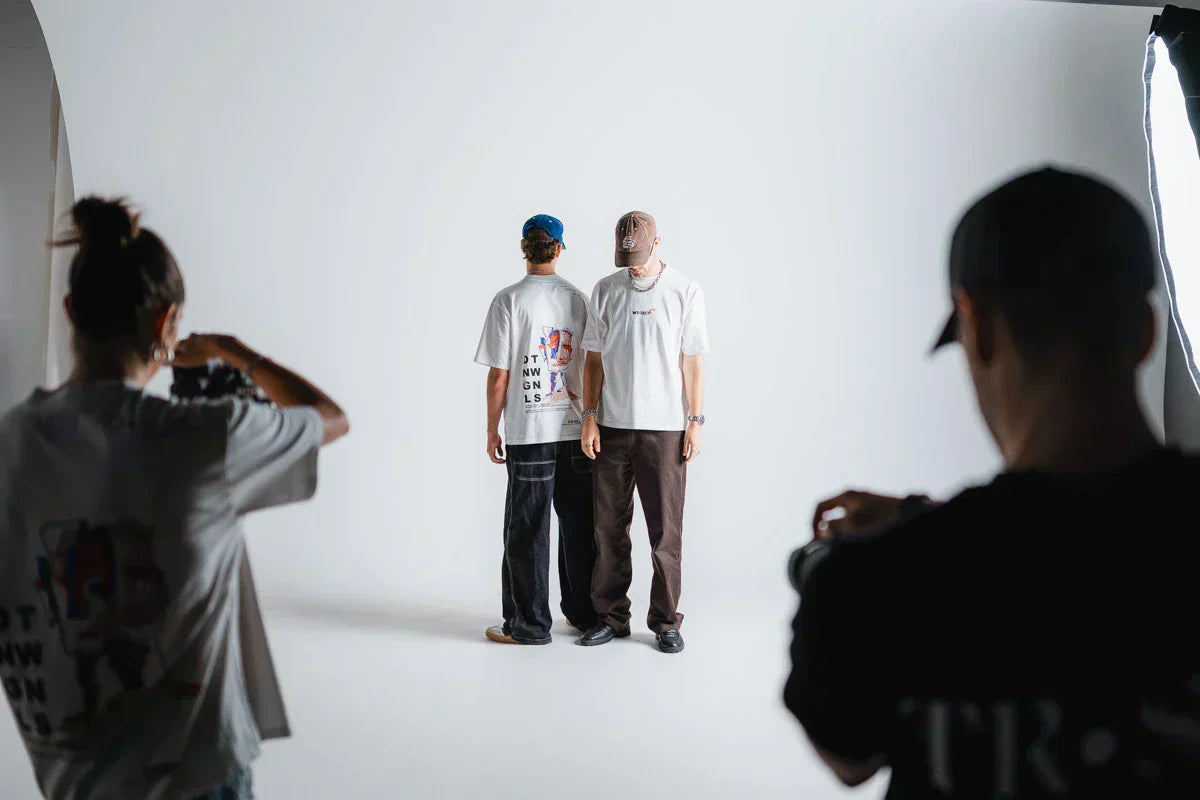 Fotoshooting der WE•TRST x Dangel Twins Kollektion im Studio – die Dangel Twins im Fokus, Fotograf:innen links und rechts, cleanes weisses Set mit Softbox.