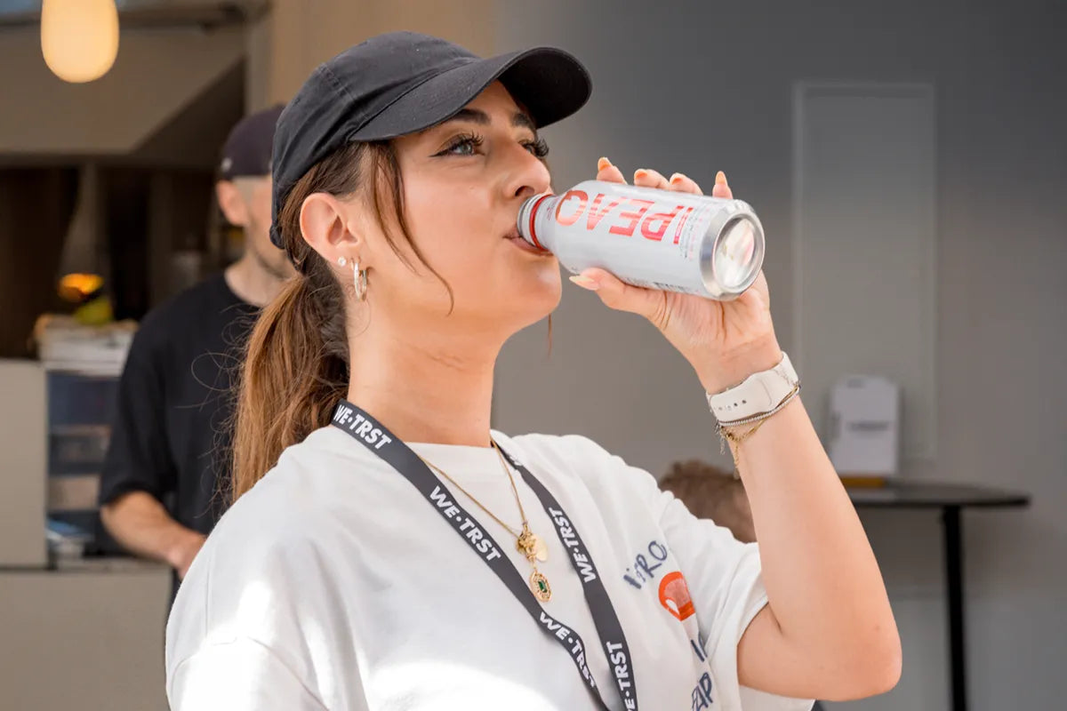 Frau mit WE•TRST-Shirt und Lanyard trinkt eine PEAQ Hydration Dose beim WE•TRST Run Club – Fokus auf Community, Sport und Schweizer Performance Water.