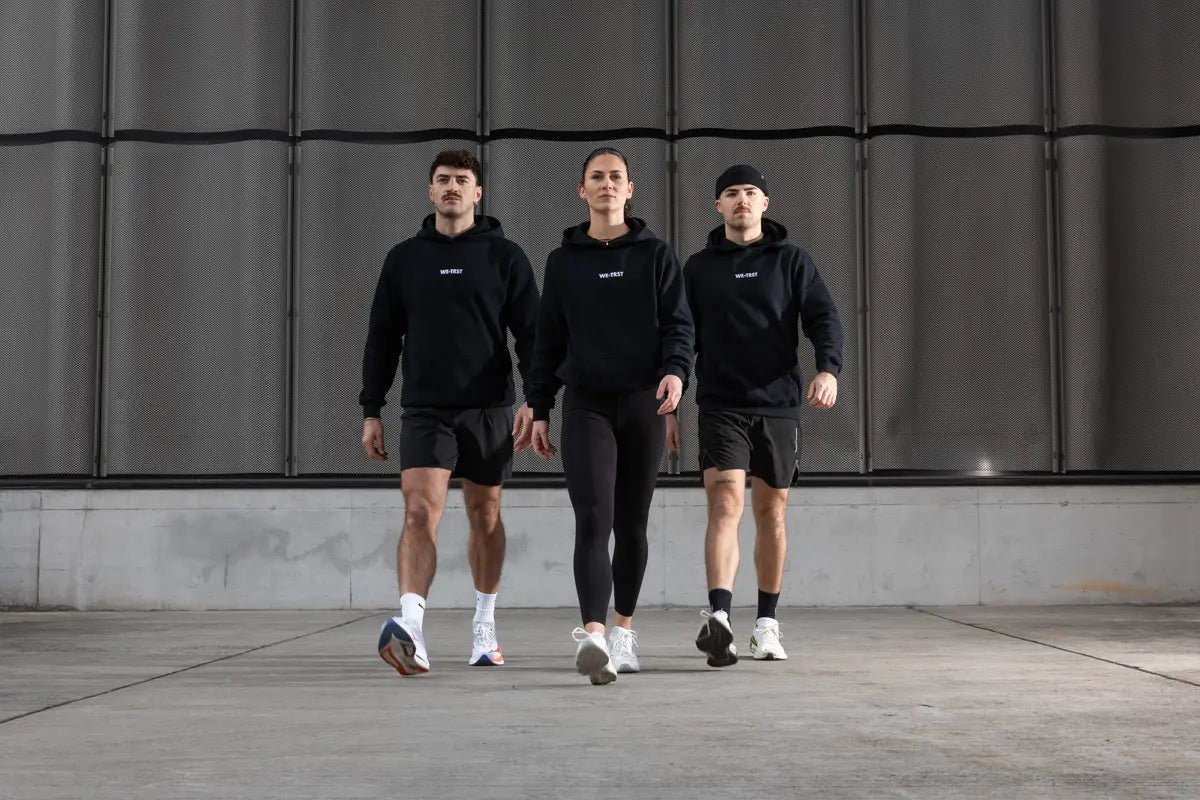 WE•TRST Run Club Community – drei Athlet:innen in schwarzer Performance Streetwear unterwegs im urbanen Raum