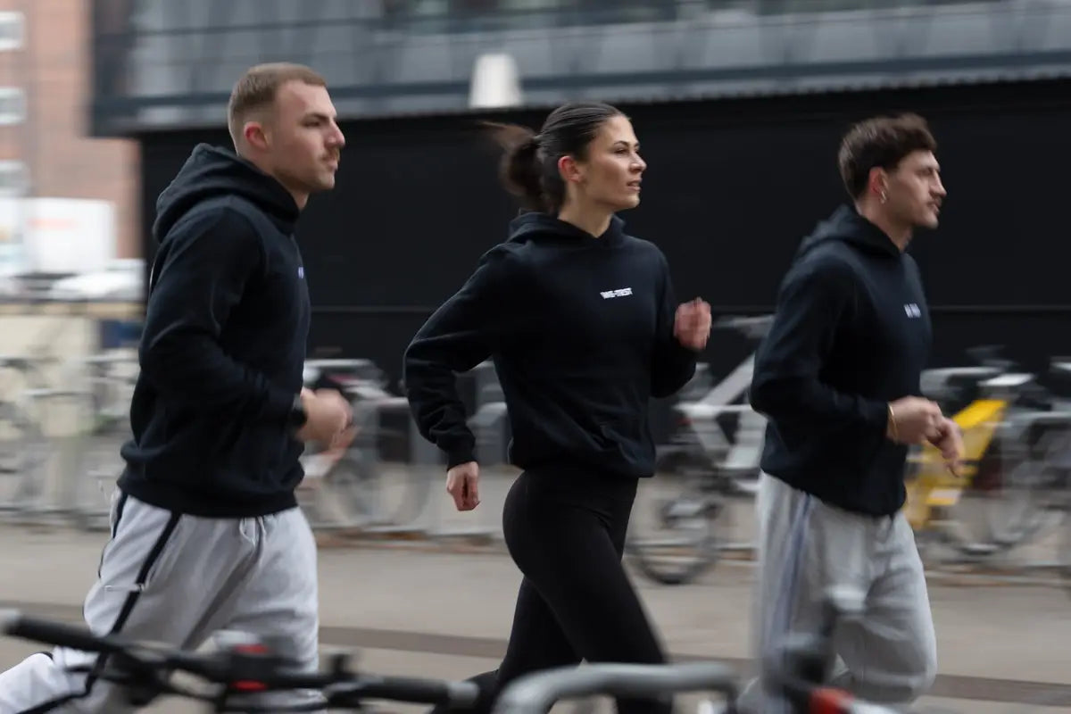 WE•TRST Run Club – drei Läufer:innen in schwarzer WE•TRST Streetwear beim Urban Running in der Stadt, Community-Run mit Fokus auf Bewegung und Zusammenhalt