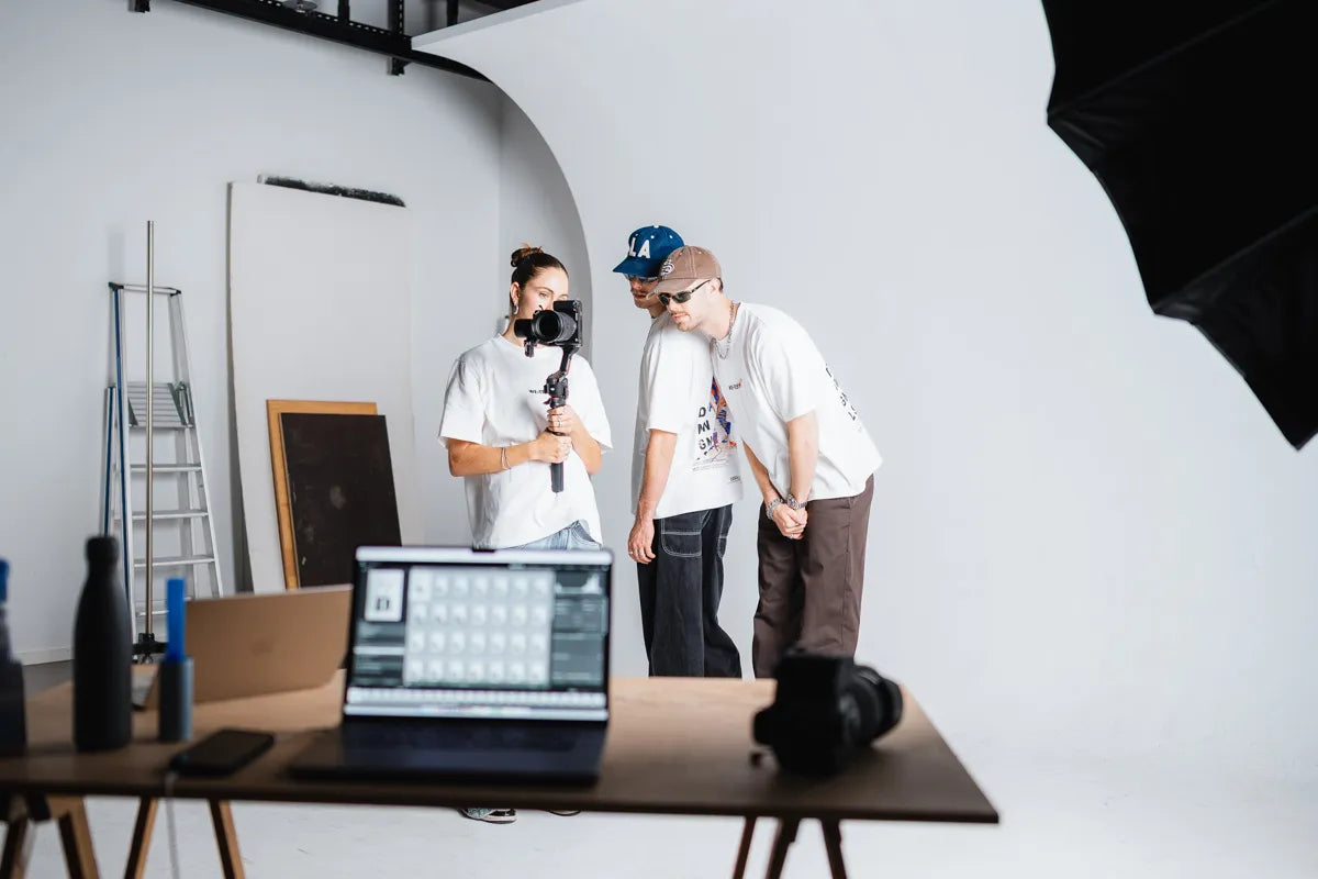 Behind-the-Scenes im Fotostudio: Die Dangel Twins und Arina Luisa mit WE•TRST x Dangel Twins T-Shirts begutachten das Ergebnis eines Shootings mit Kamera und Gimbal.