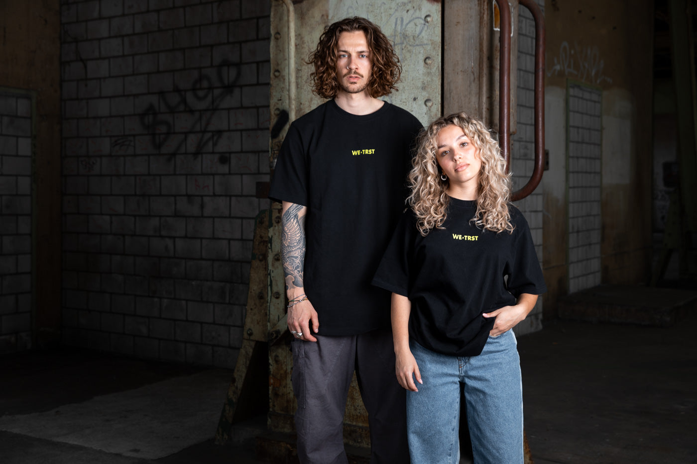 Ein Mann und eine Frau stehen mit einem WE•TRST-Shirt Modell. 