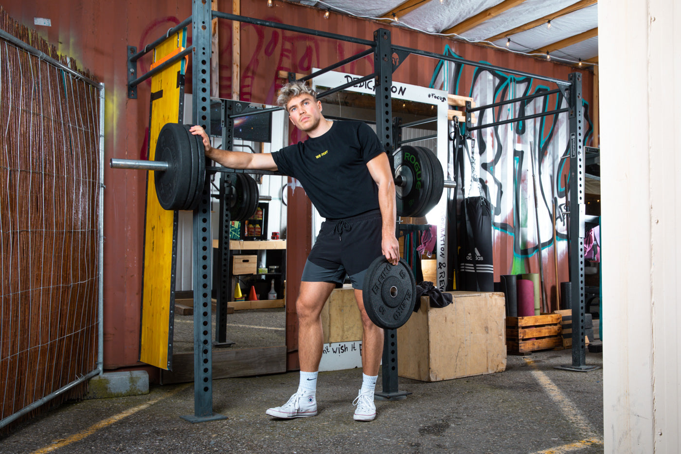 Ein Mann trainiert intensiv im Fitnessstudio und stellt seine Stärke und Entschlossenheit zur Schau. Gekleidet in ein sportliches T-Shirt von WE•TRST, zeigt er seine Unterstützung für Zusammenarbeit und Vertrauen.