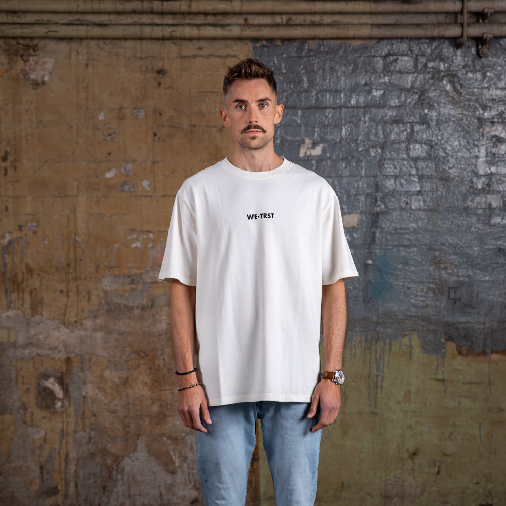 Vorderansicht des WE•TRST „Driven by Trust“ Oversized-T-Shirts in Off-White mit minimalistischem Branding und entspannter Passform.