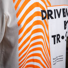Nahaufnahme des Rückendrucks auf dem WE•TRST-T-Shirt „Driven by Trust“ mit leuchtend orangefarbenen Wellenmustern und Typografie.