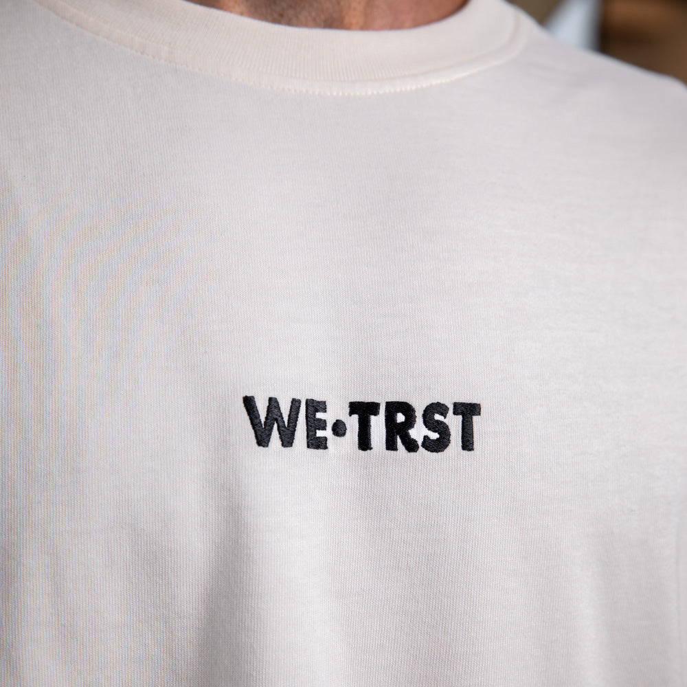 Nahaufnahme des gestickten WE•TRST-Logos auf der Vorderseite des übergroßen T-Shirts „Driven by Trust“, das die hochwertige Verarbeitung betont.