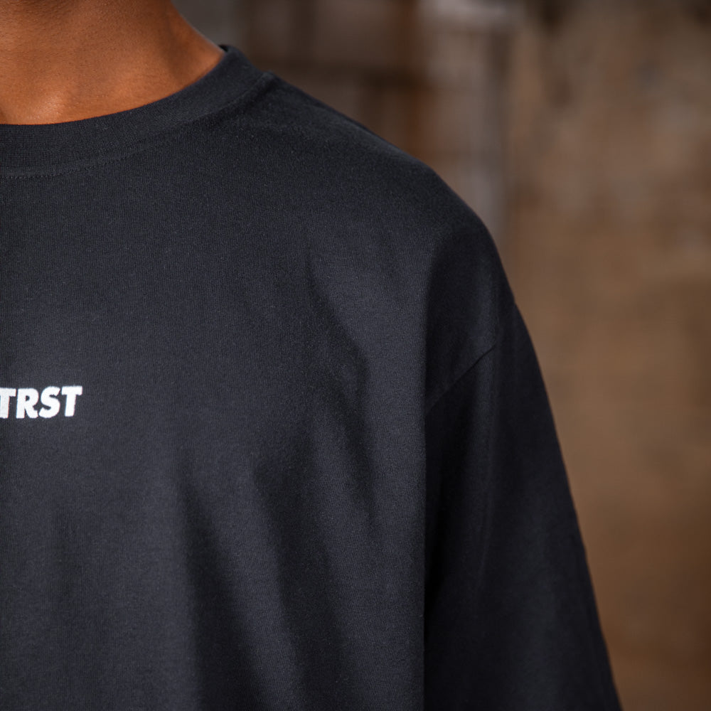 Nahaufnahme des WE•TRST-Logos auf dem schwarzen Special-Edition-T-Shirt, das das minimalistische Design der Vorderseite betont.